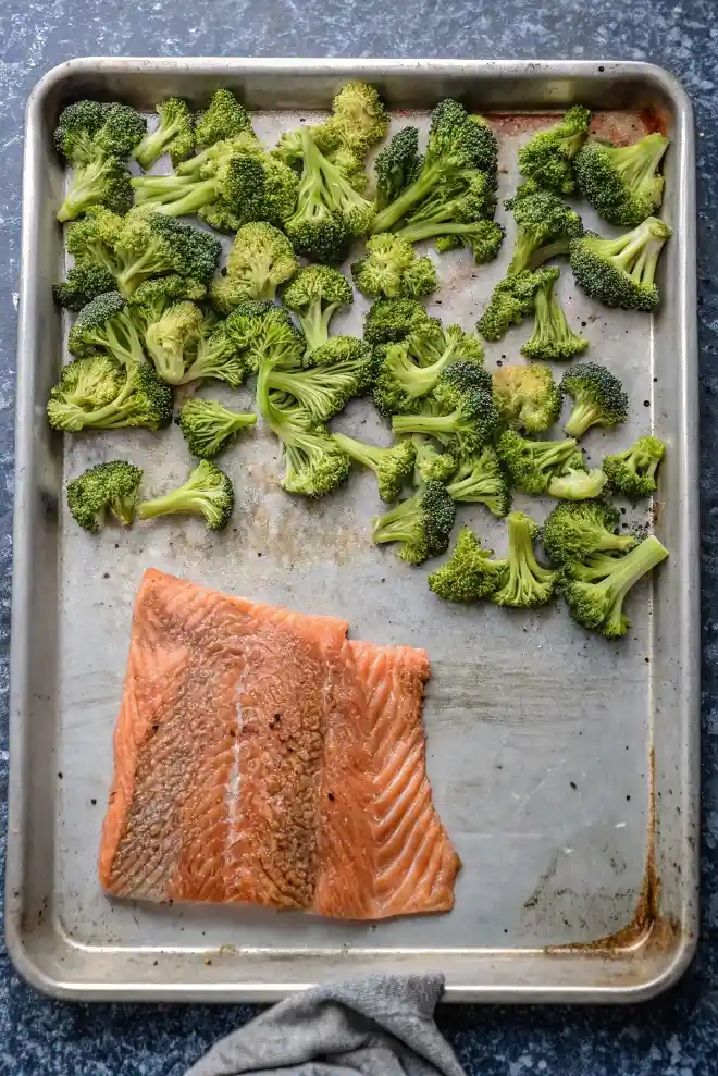 Raw salmon fillet and fresh broccoli florets arranged on a baking sheet before roasting